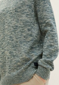 Maglione lavorato a maglia in un motivo blu e crema melangiato. Polsini e orlo a costine, con un piccolo etichetta sul lato. Texture morbida.
