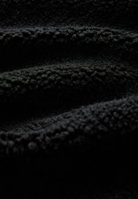 Czarny polarowy materiał o miękkiej, teksturowanej powierzchni z falistymi fałdami i lekko matowym wykończeniem, podkreślający głębię i ciepło.