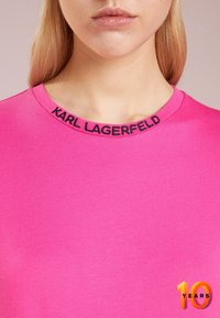 Heller pinkfarbener T-Shirt mit rundem Ausschnitt. "KARL LAGERFELD" ist in Schwarz um den Kragen gestickt. Weiches, glattes Stoffgefühl.