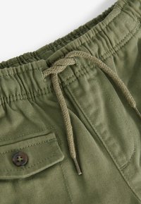 Grüne Baumwollshorts mit elastischem Bund, verstellbarem Kordelzug und einer Knopf-Seitentasche. Glatte Textur und lockere Passform.