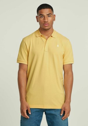 Polo shirt giallo in cotone con pattina a due bottoni, maniche corte e un piccolo logo sul petto. Tessuto liscio, vestibilità standard.