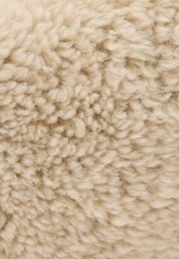 Štruktúrovaná béžová tkanina s mäkkými, chĺpkami s kučeravým, slučkovým povrchom, vytvárajúcimi príjemný vzhľad. Ideálna na čalúnenie alebo dekorácie.