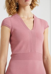 Rosa gestricktes Kleid mit V-Ausschnitt, kurzen Ärmeln und vertikalen Rippenmustern entlang des Oberteils und der Taille für eine strukturierte Textur.