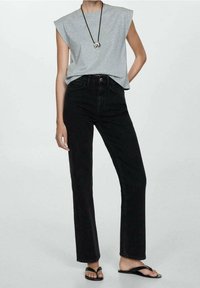 T-shirt sans manches gris, jean en denim noir taille haute, sandales plates noires et collier pendentif au design minimaliste.