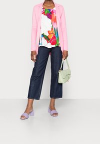 Růžový sak na míru, barevný květinový top, tmavé široké džíny, lila sandály na blokovém podpatku a světle zelená kabelka.