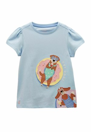 Chemise bleu clair à manches courtes avec des épaules bouffantes, présentant deux chiens de dessin animé en maillots de bain, lunettes de soleil, avec le texte « HOT DOGS ».