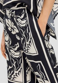 Schwarze und cremfarbene gemusterte Hose mit floralem Design, ausgestattet mit einer taillierten Taille, seitlichen Taschen und einer glatten Textur.