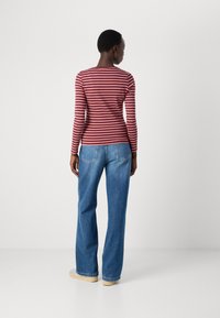 Camicia a maniche lunghe a righe rosse e rosa abbinata a jeans a vita alta blu a gamba larga. Tessuto morbido, vestibilità rilassata. Nessun motivo o accento prominente.