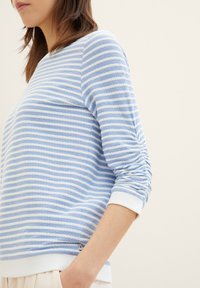 Sweat-shirt rayé bleu clair et blanc avec un col rond, en tissu texturé, et des manches froncées, comportant un ourlet et des poignets en côtes blancs.