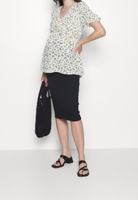 Blouse blanche à motifs floraux verts, col en V et manches courtes bouffantes, associée à une jupe crayon noire et des sandales noires à lanières.