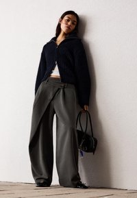 Navy ribbed knit zip-up sweater, white crop top, high-waisted gray wide-leg trousers with unique draping and a black handbag.