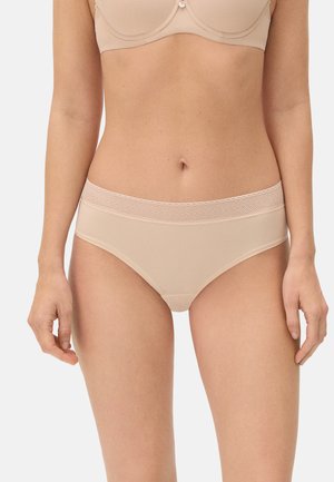 Mujer con braguitas sin costuras de corte alto en beige con una cinturilla texturizada y sujetador a juego, vista desde medio torso hasta la parte superior de los muslos.