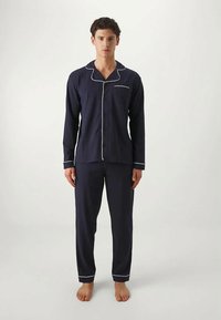 Navy blue pajama set made of soft fabric, featuring a button-up shirt with white piping and matching pants. Simple design, relaxed fit.