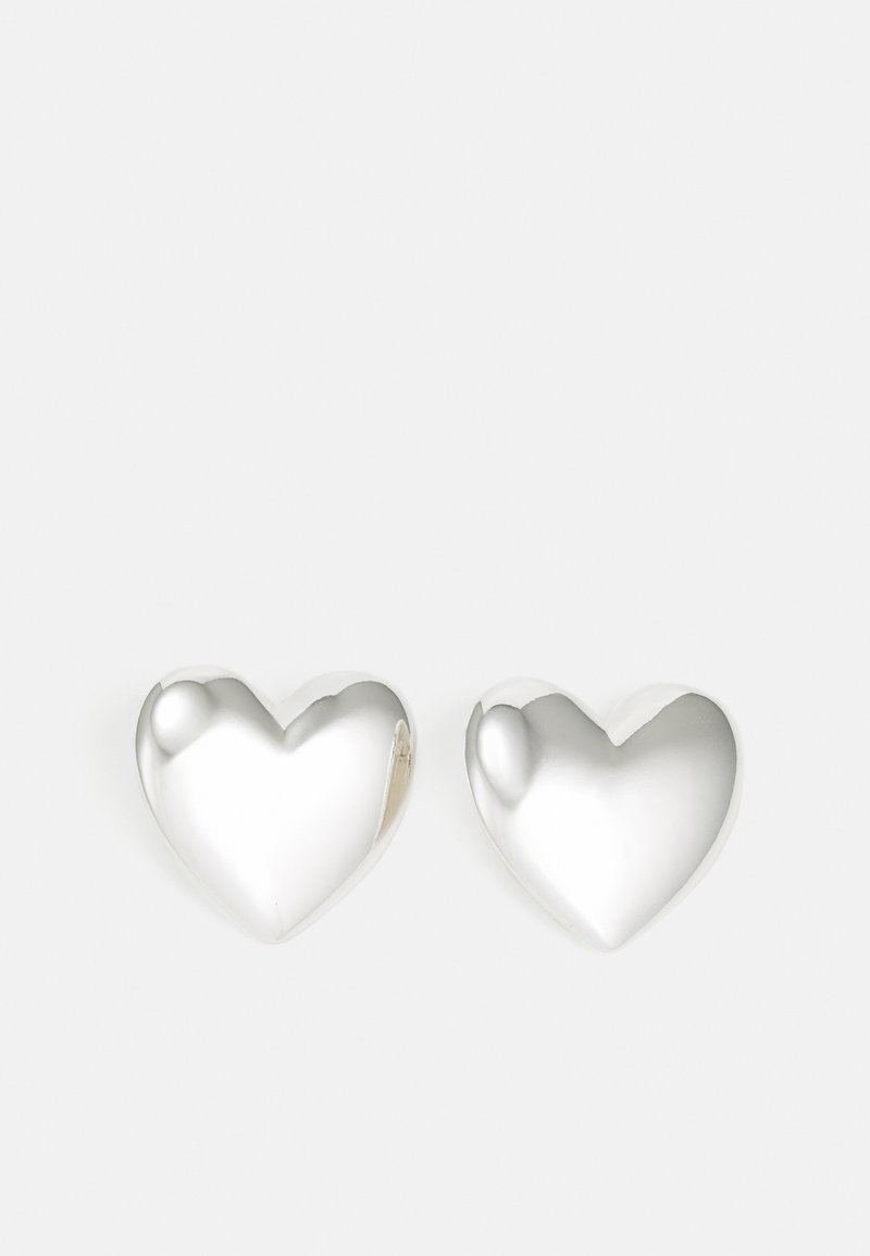 Pendientes de plata en forma de corazón con una superficie lisa y reflectante. Bordes redondeados y un suave surco en la parte superior. Diseño ligero.