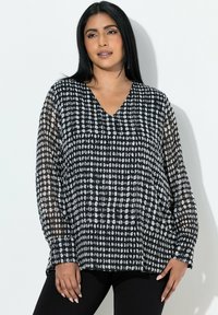 Sort-hvid mønstret bluse med V-hals, lange ærmer og let gennemsigtigt stof, der viser et geometrisk design af prikker og ovaler.