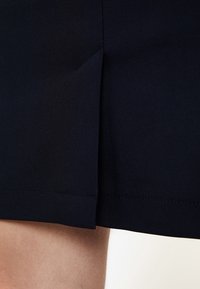 Tissu de jupe bleu marine avec une texture lisse, présentant une fente sur le côté. L'ourlet est uni avec des coutures soignées, mettant en valeur un design simple et ajusté.