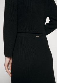 Svart ribbat stickat tröja och kjolset, försett med långa ärmar och en smal passform. Notabelt guldhardware som accent på kjolens midjeband.