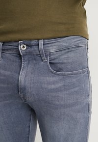 Jeans de mezclilla azul claro con un diseño clásico que incluye un cierre de botón, bolsillos frontales y una textura sutil de desgastes.