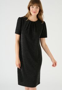 Abito nero con maniche corte, caratterizzato da un colletto plissettato, tessuto testurizzato con una leggera lucentezza e una silhouette aderente.