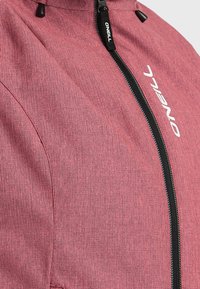 Roze textuur jasje met een hoge kraag, zwarte rits en een wit logo-detail aan de voorkant. De stof lijkt duurzaam en lichtgewicht te zijn.