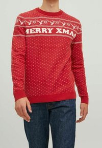 Roter Weihnachtspullover mit weißen Rentier- und Schneeflockenmuster sowie dem Text "FROHE WEIHNACHTEN" auf der Brust, getragen mit blauer Jeans.