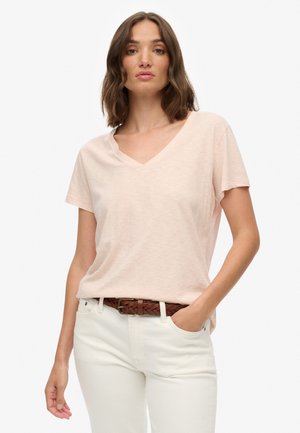 Jasnoróżowy t-shirt z dekoltem w serek, wykonany z miękkiego materiału, z krótkimi rękawami, zestawiony z białymi spodniami i brązowym plecionym paskiem.