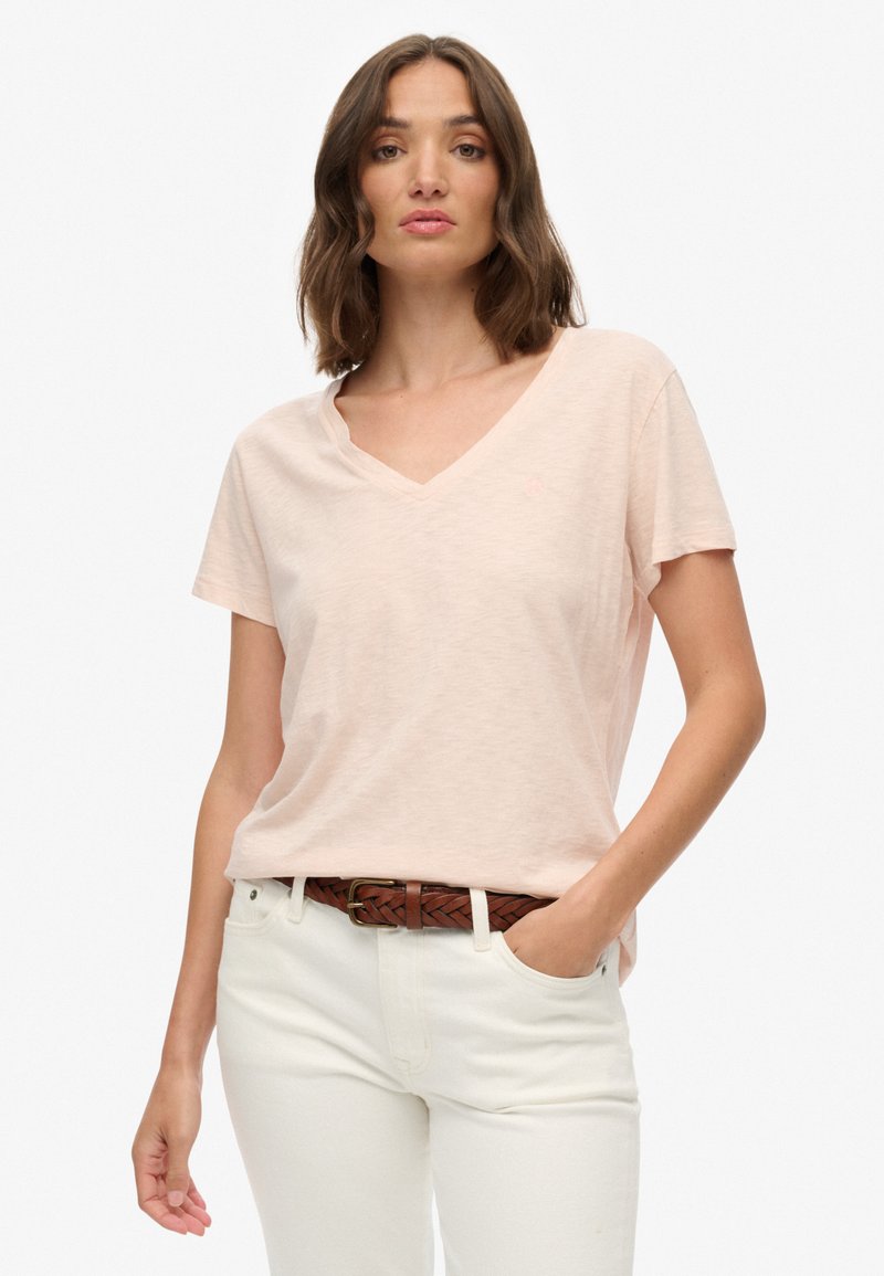 T-shirt rosa chiaro a scollo a V realizzato in morbido tessuto, con maniche corte, abbinato a pantaloni bianchi e una cintura intrecciata marrone.