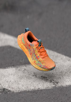 Pantof sport portocaliu aprins cu partea superioară texturată, modele multicolore și talpă ușoară, având o etichetă albastră la călcâi și șireturi portocalii.