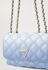 Borsa a tracolla di pelle trapuntata blu chiaro con tracolle in catena dorata e un logo triangolare argento sul davanti. Presenta una forma rettangolare compatta.