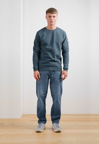 Sudadera azul oscuro con mangas largas y cuello redondo, combinada con jeans azul claro y zapatillas grises. Diseño simple sin patrones.