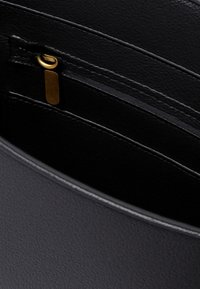 Wnętrze czarnej skórzanej torebki ukazuje teksturowany materiał, zamek błyskawiczny z złotą zawieszką oraz liczne kieszonki na karty z przeszytymi detalami.