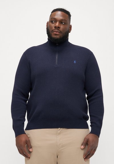 Jersey de punto acanalado en azul marino oscuro con un cuello alto y media cremallera. Presenta un pequeño logo azul en el pecho y mangas ajustadas.