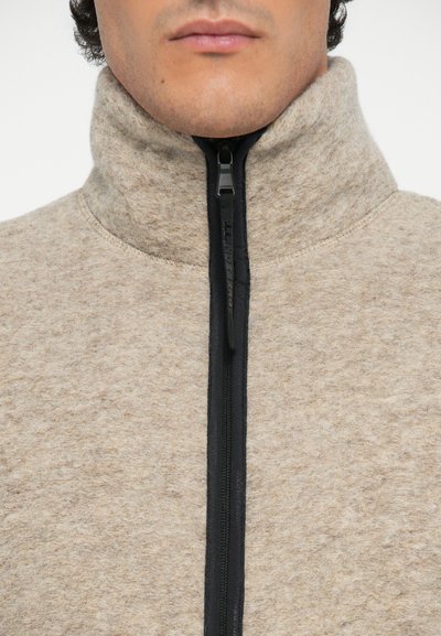 Beige fleece jacket with a high collar and black zipper. The texture is soft and warm, featuring smooth seams along the edges.