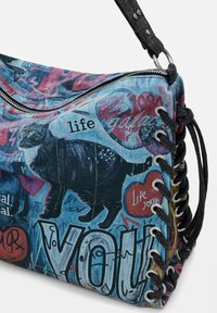 Mehrfarbige Denim-Tasche mit grafischen Drucken, darunter eine schwarze Katze und Text, mit silbernem Reißverschluss und geflochtenen schwarzen Trägern.