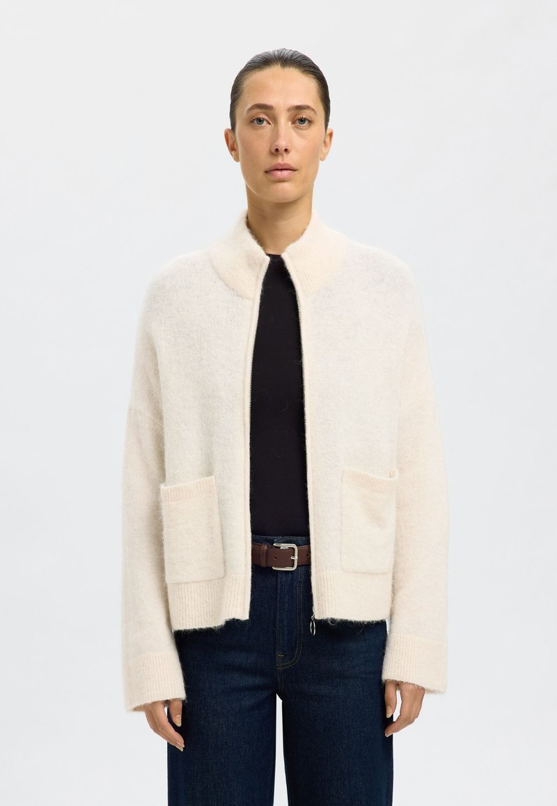 Crème-kleurige cardigan van zacht, textuurstof met een hoge kraag en twee voorzakken, contrasterende geribbelde manchetten en een ontspannen pasvorm.