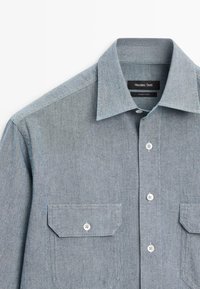 Světle modrá košile na knoflíky s špičatým límečkem a dvěma předními kapsami s klopami, označená Massimo Dutti, vyrobená v Turecku.