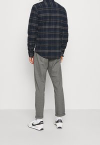 Camicia a quadri nei toni del blu e grigio con colletto a bottone, abbinata a pantaloni della tuta grigi. Sneakers bianche con dettagli neri e logo.