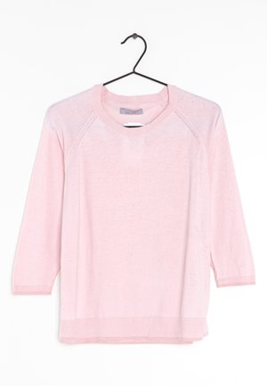 Jasnoróżowy sweter z długim rękawem, o okrągłym dekolcie i ściągaczami na mankietach oraz u dołu, zawieszony na czarnym wieszaku na białym tle.