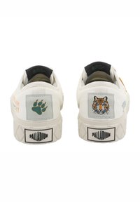 Tênis de lona branca com costuras padronizadas, apresentando uma pata verde e um gráfico de tigre no calcanhar, sola texturizada e logótipo.