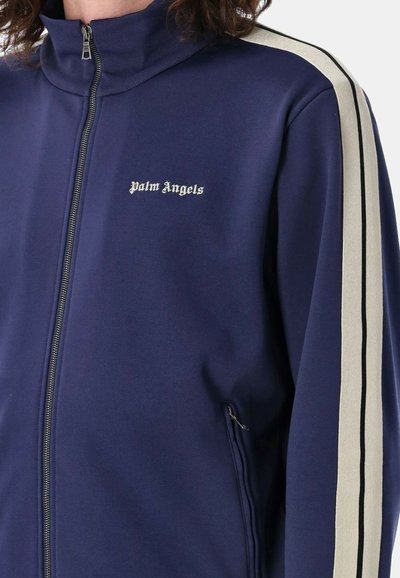 Giacca da track navy con zip, realizzata in tessuto morbido, con strisce nere e crema sulle maniche e logo "Palm Angels" in bianco.