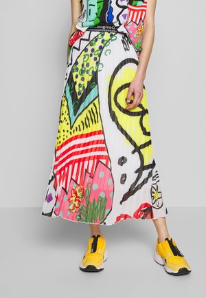 Personne portant une jupe colorée à motifs abstraits et des baskets jaunes, debout devant un fond gris uni.