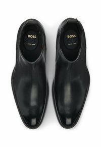 Scarpe slip-on in pelle nera con finitura lucida, punta a forma di mandorla e dettagli elastici laterali. Soletta interna etichettata "BOSS", realizzata in Italia.