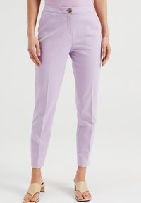 Fialové přizpůsobené kalhoty s hladkým povrchem, s předním zapínáním na knoflík,zužujícími se nohavicemi a bočními kapsami. Nošeny s béžovými sandály na klínku.