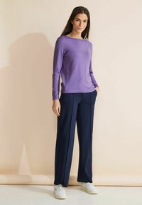 Ljuslila långärmad topp i kombination med marinblå vida byxor och vita sneakers. Slät tyg och klassisk rund halsringning.