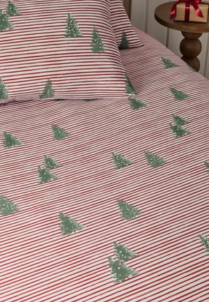 Bett mit weißen und rot gestreiften Bettlaken und Kissenbezügen mit grünen Weihnachtsbaum-Mustern, neben einem hölzernen Beistelltisch mit einem eingepackten Geschenk.