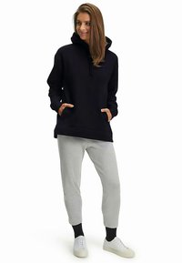 Felpa blu navy con cappuccio e tasche a marsupio, abbinata a pantaloni grigi chiaro a gamba affusolata e sneaker bianche, con una vestibilità rilassata e casual.