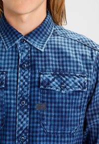 Blå rutiga flanellskjortor med knapp-up framsidan, spridande krage, två bröstfickor och en liten logopatch på vänster ficka.