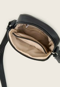 Sac rond en cuir noir à bandoulière avec fermeture éclair, présentant un intérieur en tissu beige et un compartiment zippé.