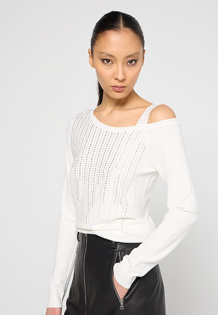 Weißes Langarmoberteil im Off-Shoulder-Design, verziert mit silbernen Strasssteinen in vertikalen Mustern, kombiniert mit einem schwarzen Lederrock.