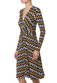 Vestido de manga larga tipo envoltura con un patrón en chevrón en negro, blanco y naranja. Fabricado con un tejido elástico, tiene una cintura ajustada y una falda acampanada.